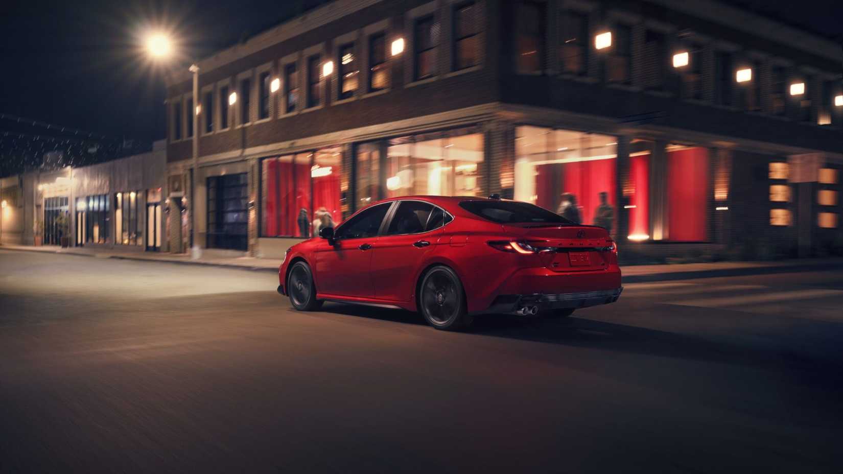 Dynamic rear 3/4 shot of a red 2026 Toyota Camry Nightshade driving through a city.