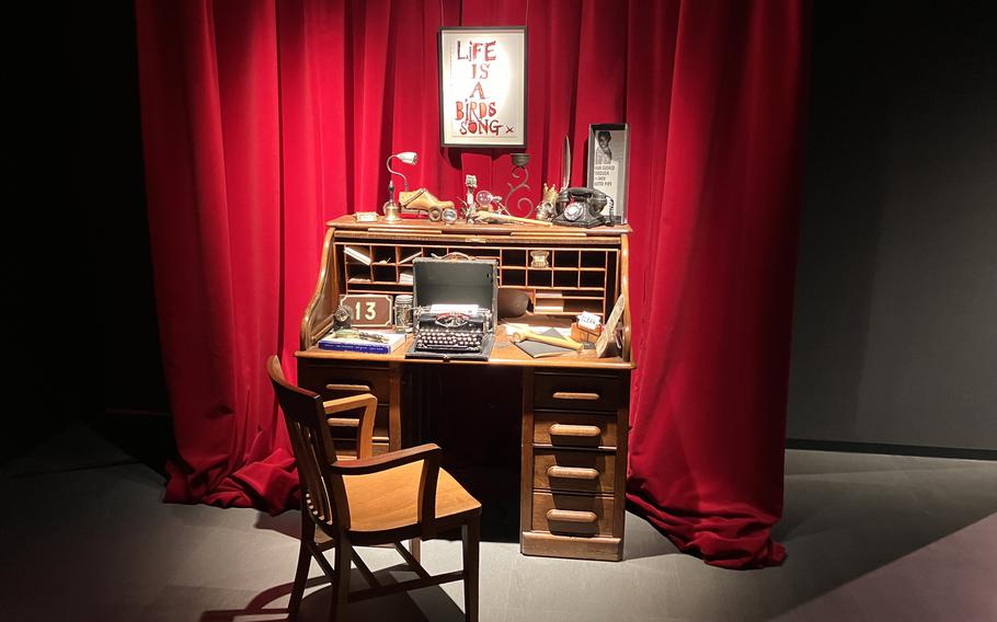 A cluttered desk sits in front of a red curtain.