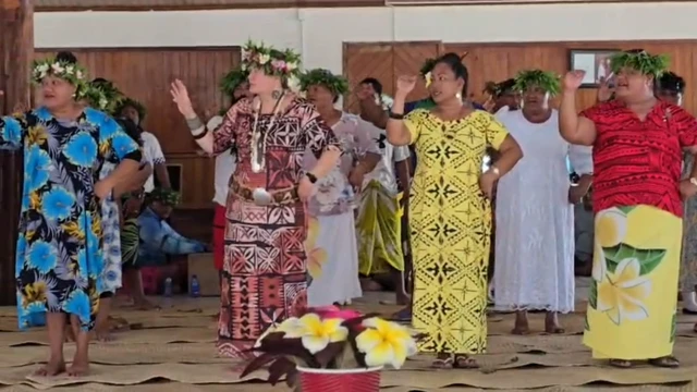 Four people in brightly coloured dressed dance in a hall. They all have flowers in their hair