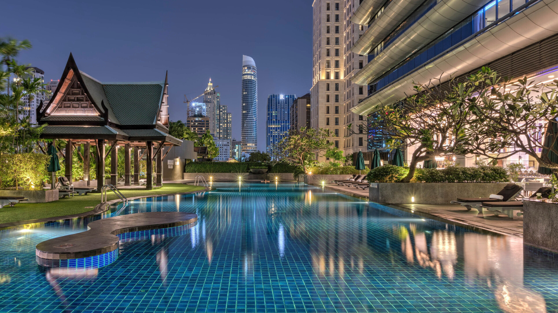 The pool at the Athenee hotel in Bangkok at night with the lit up city skyline behind it 