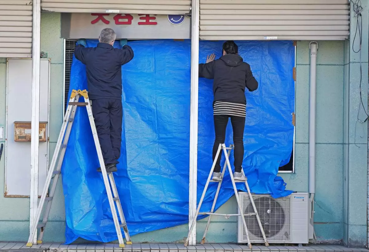 People cover the broken glasses with a blue sheet at a beauty salon in Hachinohe, Aomori prefecture, northern Japan Tuesday, Dec. 9, 2025, following a powerful earthquake on late Monday. (Kazuki Kozaki/Kyodo News via AP)