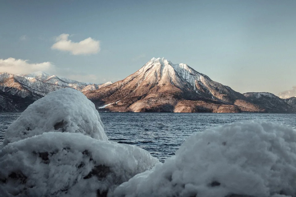 A calm sea at the edge of a snow-peaked mountain with a low ice wall framing the view.