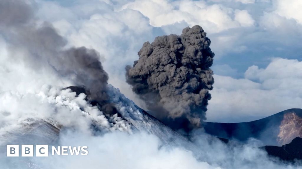 Snow-capped Etna erupts as skiers use its slopes A black plume erupts from Mt Etna with clouds behind it.