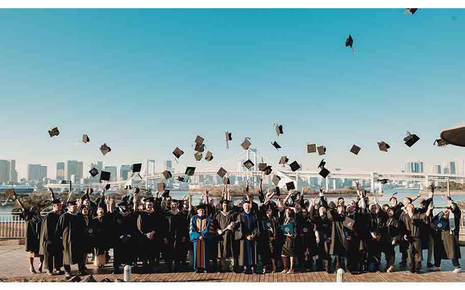 Embry-Riddle Aeronautical University Class of 2025 Graduation group photo, graduation cap toss, Odaiba’s Rainbow Bridge and the Tokyo Bay in the background