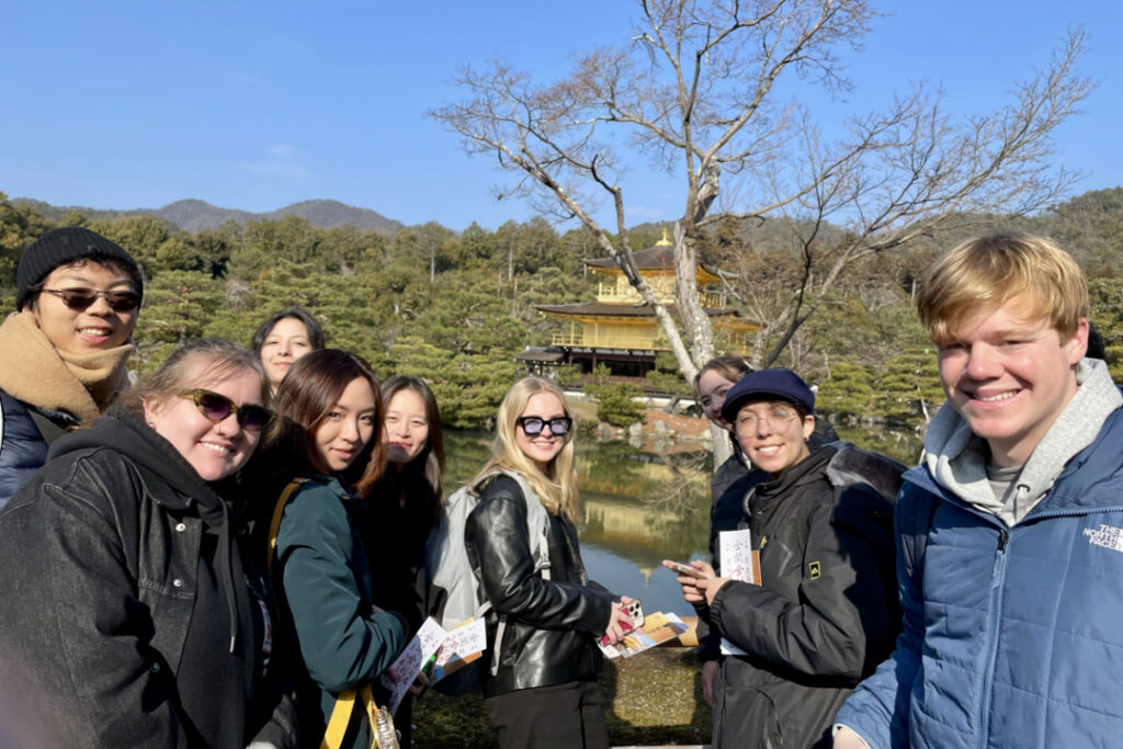 A group of people pose for a photo in front of a temple and body of water.