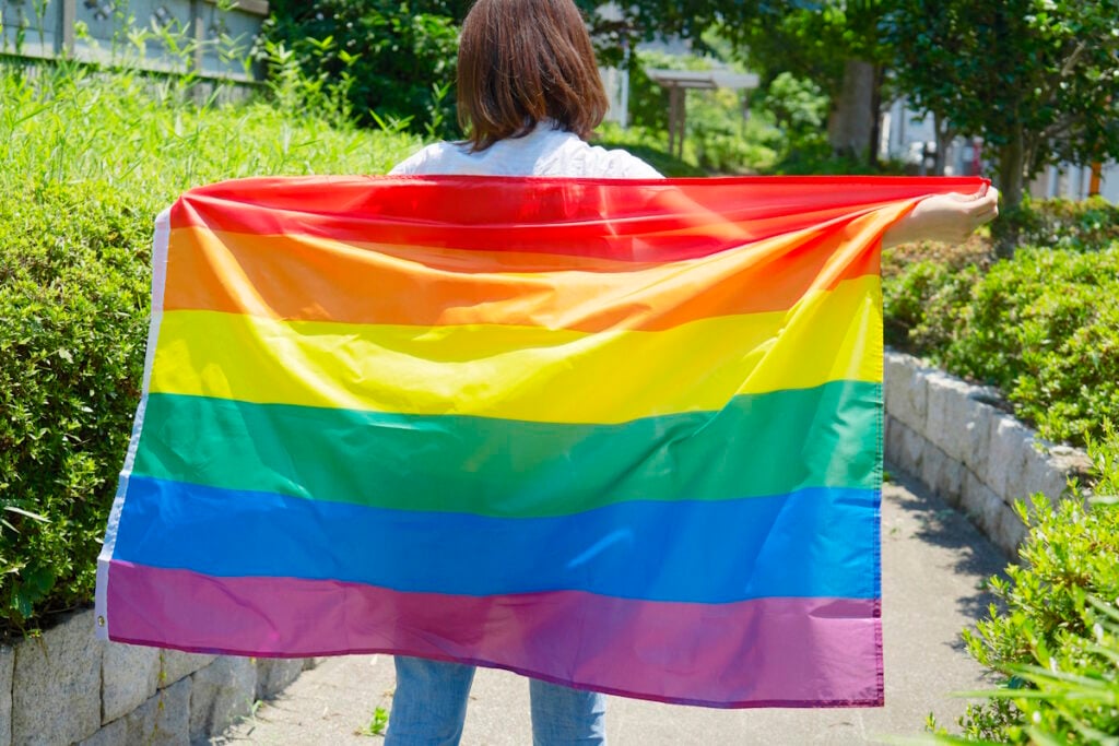 Woman holding up LGBTQ flag against her back