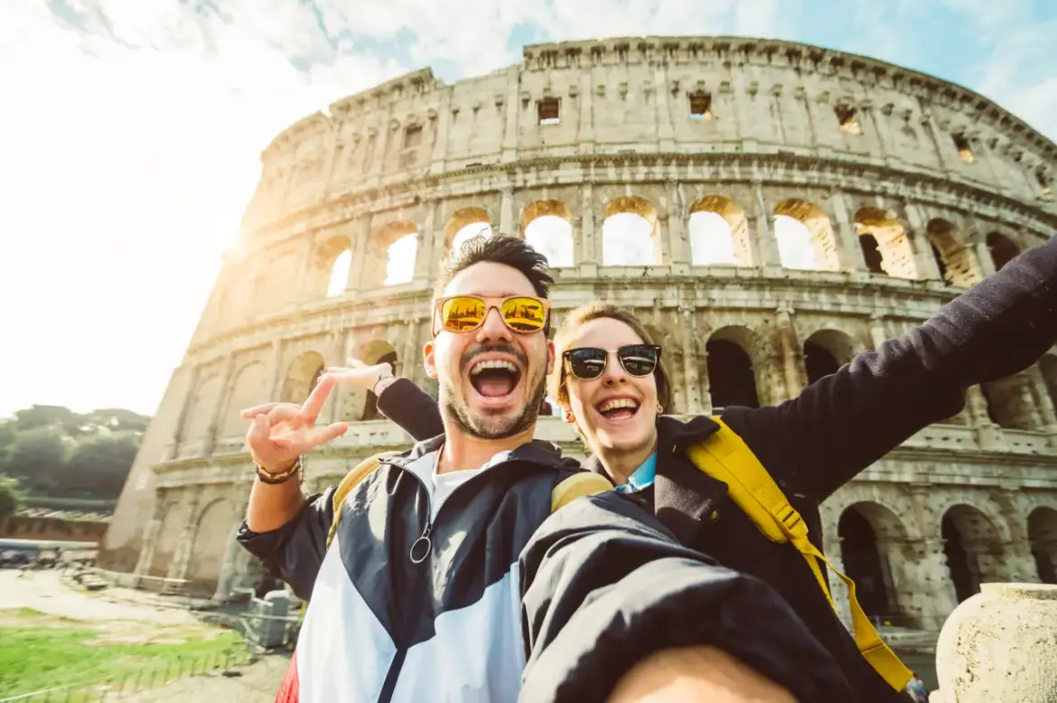 September Travel Data Shows US Arrivals Down as Americans Keep Going Abroad Happy couple taking a selfie in front of the Colosseum in Rome, Italy.