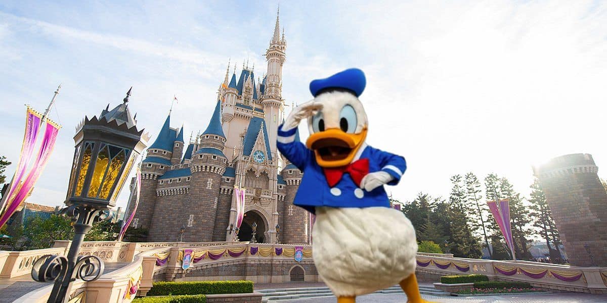 A cheerful Donald Duck greeting visitors in front of the iconic fairy tale castle on a bright sunny day at Tokyo Disneyland.