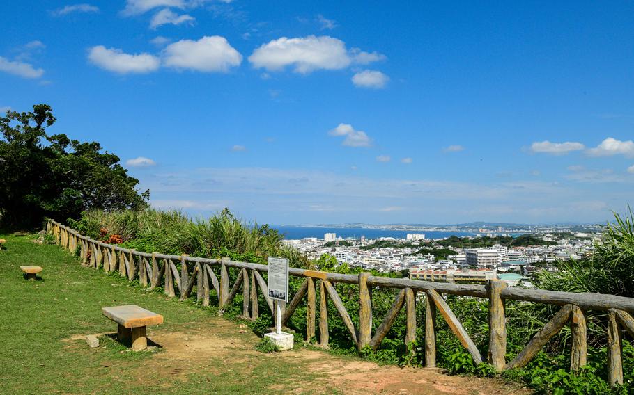A fenceline runs along a cliff edge overlooking a town on a sunny day.