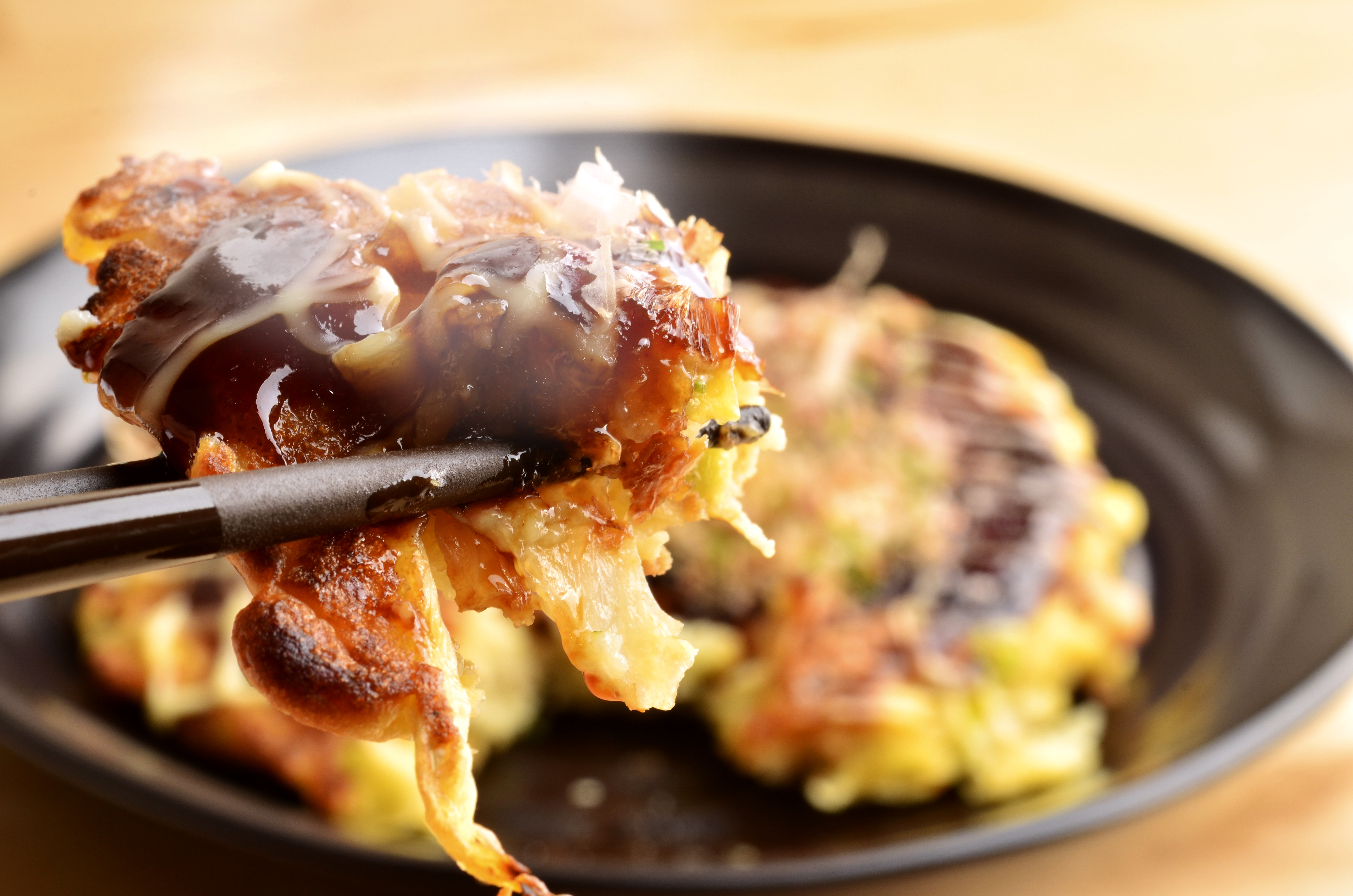 Okonomiyaki, Japanese pancake-style food, being lifted with chopsticks.