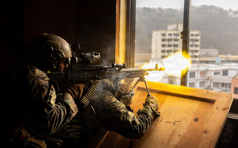 Marines fire on simulated adversary forces with an M240B machine gun from a window.