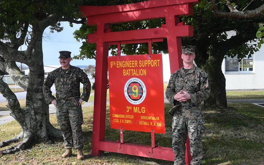 Two U.S. servicemembers stand near a sign in Okinawa, Japan.