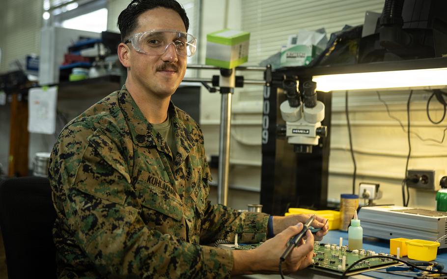 A Marine repairs a circuit board in a workshop.