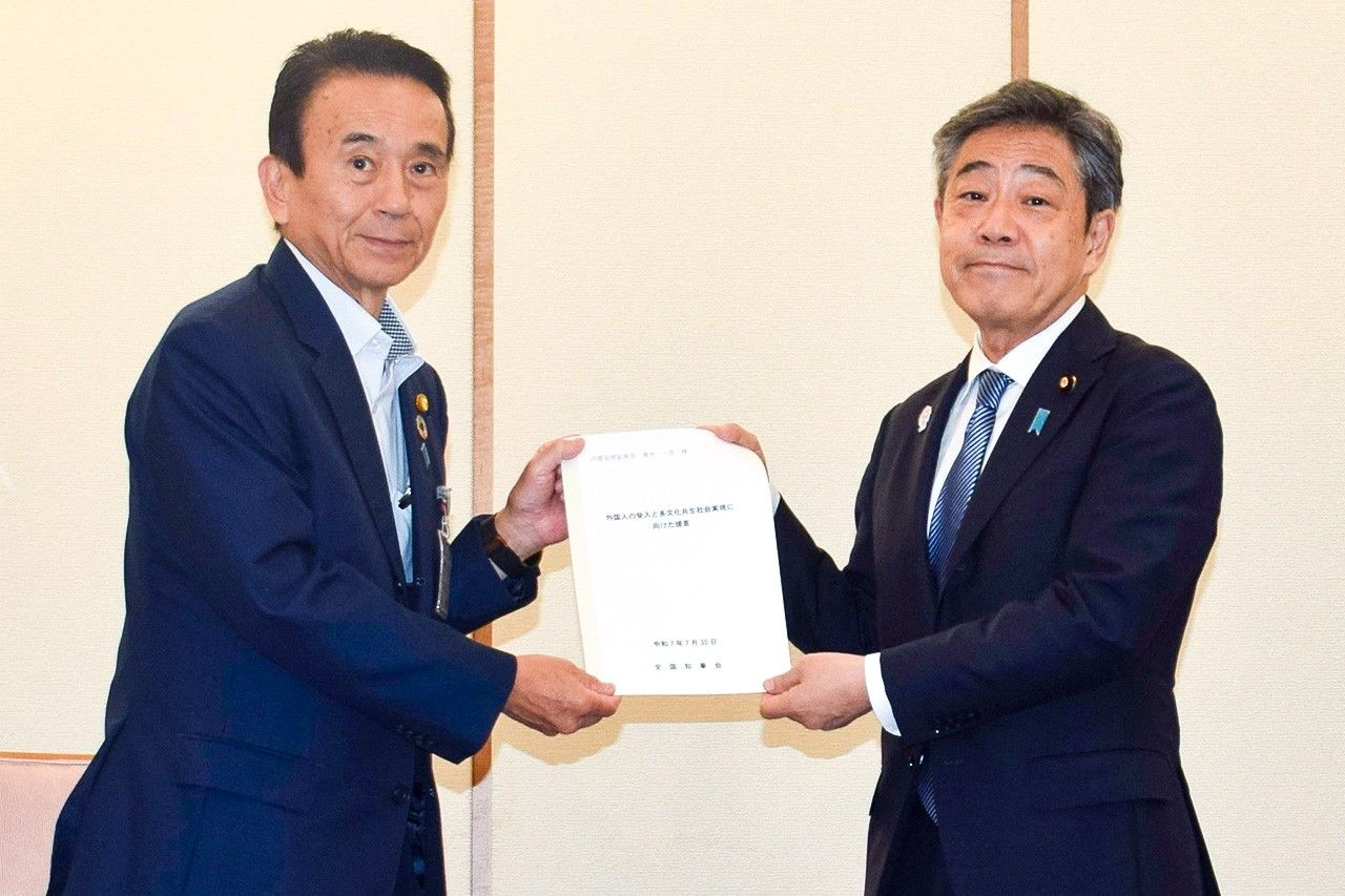 Shizuoka Governor Suzuki Yasutomo (left) handing the NGA’s proposal to Deputy Chief Cabinet Secretary Aoki Kazuhiko in Tokyo in July 2025. (© Jiji)