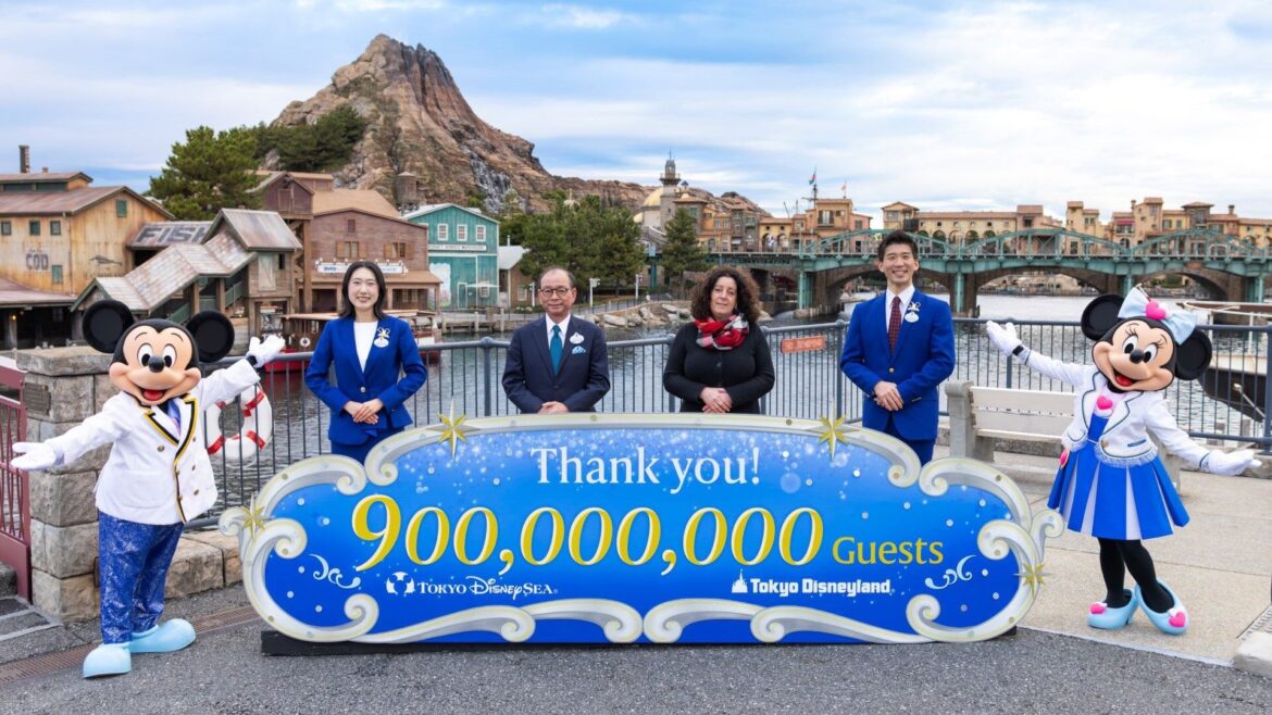 Minnie and Mickey standing with four cast members and a giant sign celebrating 900 million guests to the Tokyo Disney Resort.
