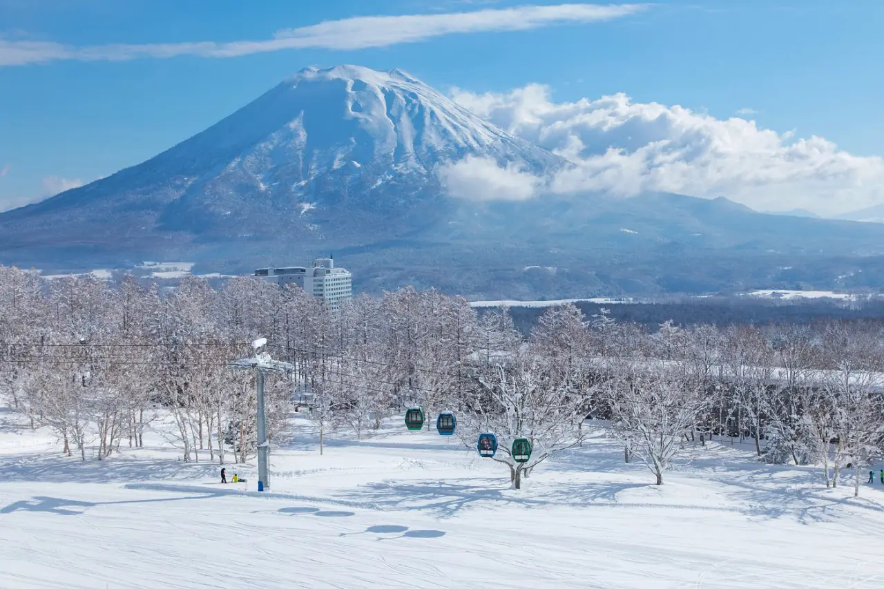 Snow-covered ski slopes with gondola cabins and Mount Niseko Annupuri rising in the background under clear blue skies.