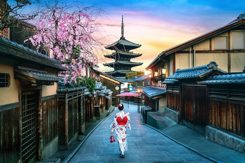 More Mexicans are visiting Japan, driven by cultural interest Beautiful sunset view of a Japanese street featuring cherry blossoms, traditional wooden buildings, and a pagoda in the background.