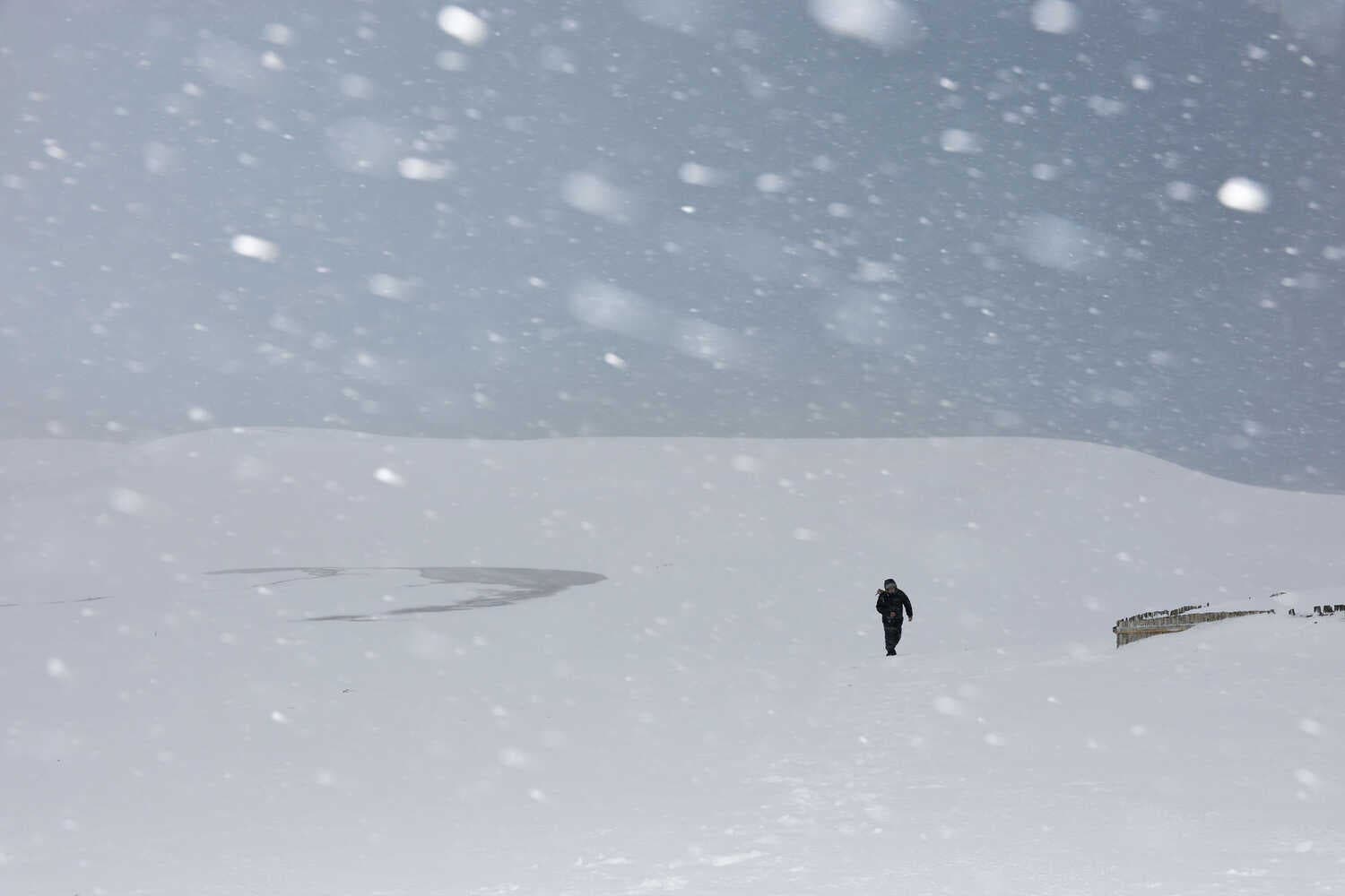 A man walking amid heavy snowfall covering sand dunes. 