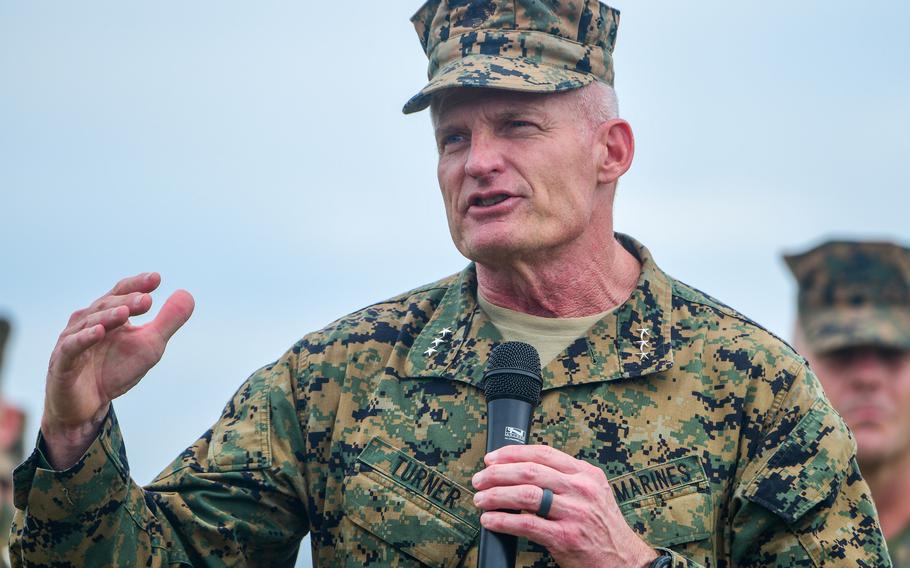Roger Turner, a three-star general, holds a microphone as he addresses the audience at a change-of-command ceremony.