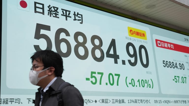 A person walks in front of an electronic stock board...