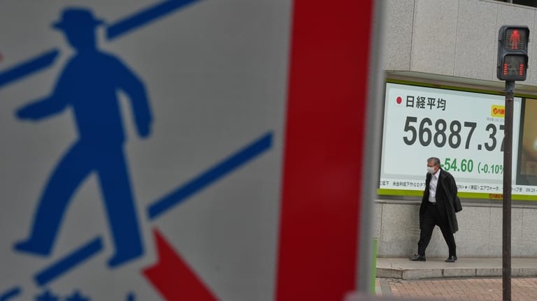 A person walks in front of an electronic stock board...