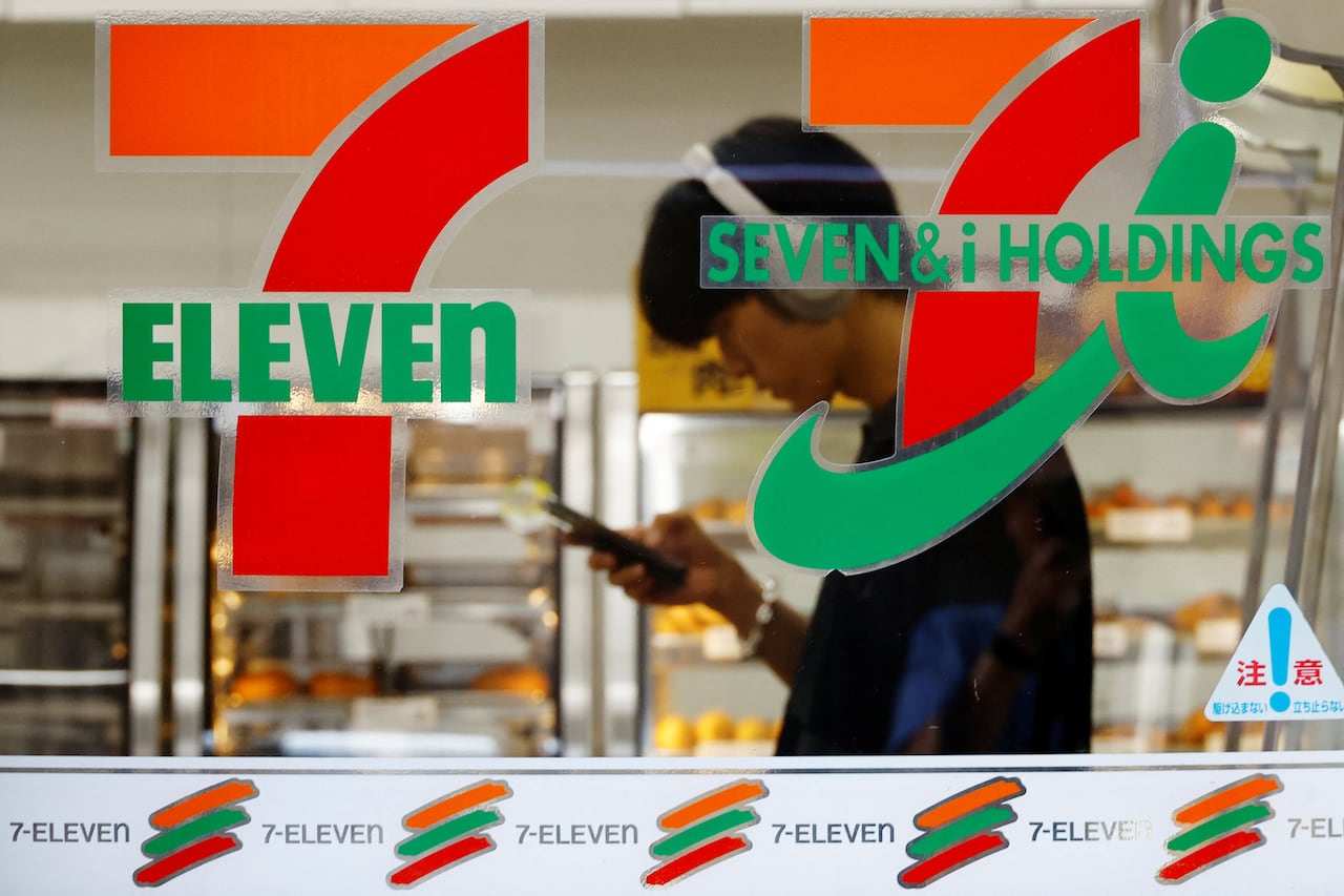 A man looks at his phone in the window of a 7-eleven store