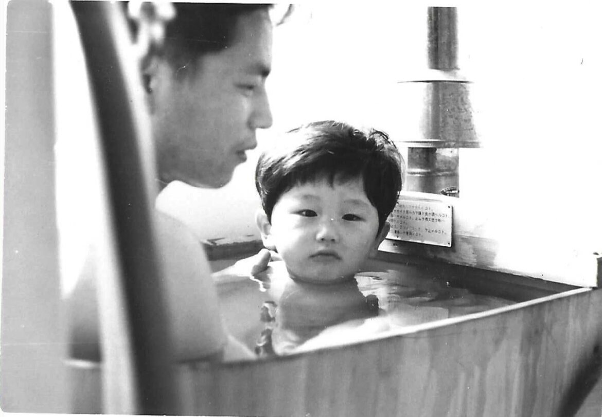 “a traditional hinoki wooden bathtub in a Showa-era public housing unit, heated by a gas-fired bath boiler”