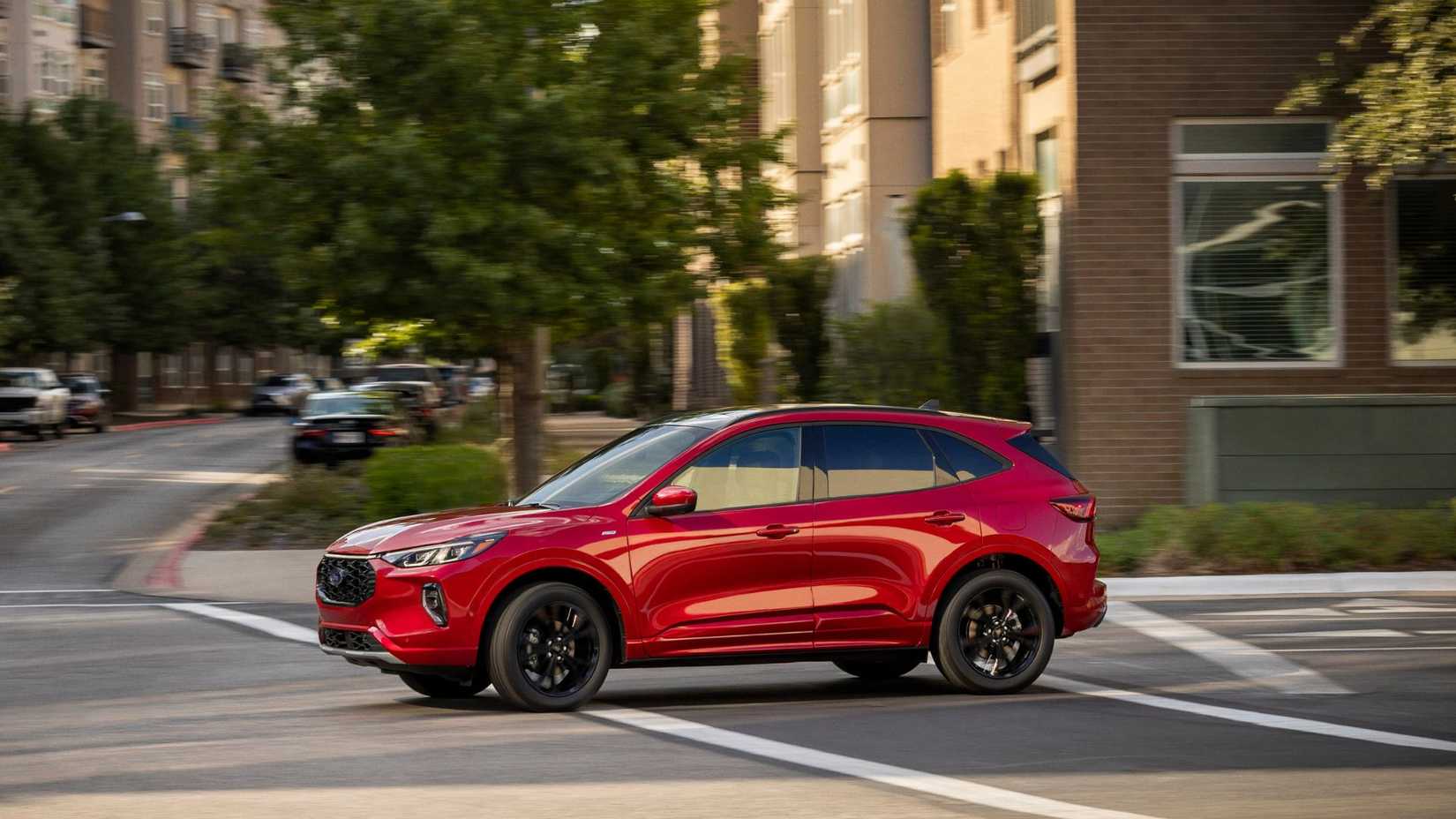 Dynamic side profile shot of a red 2023 Ford Escape ST-Line Elite driving through a city.