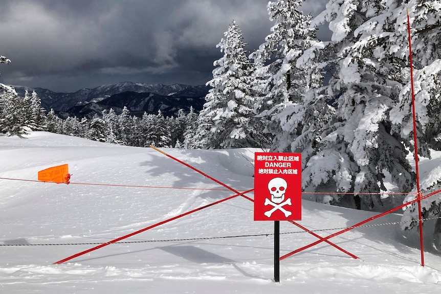 A red warning sign and red tape blocks off an area covered with thick snow as dark grey clouds hang on the horizon