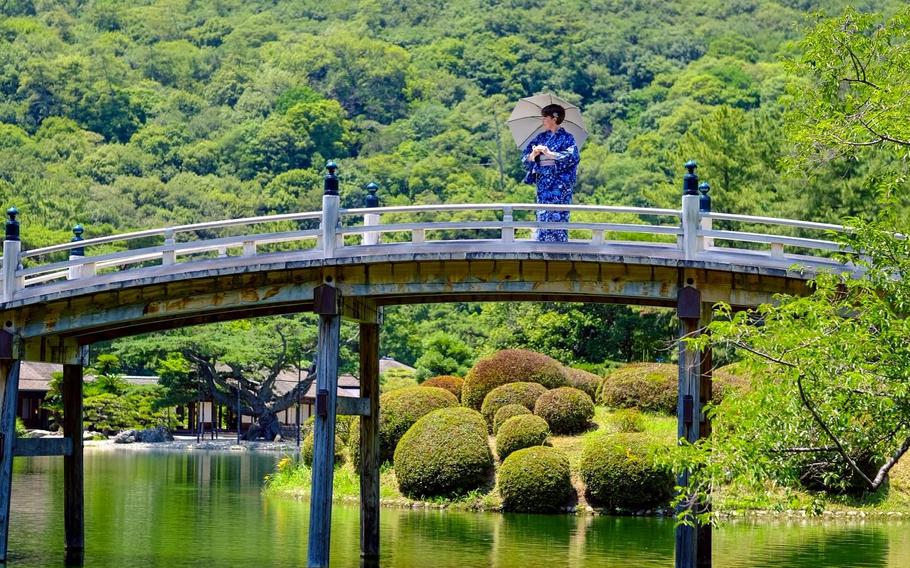 The author in a traditional Japanese cloth and using an umbrella on the bridge of Ritsurin.