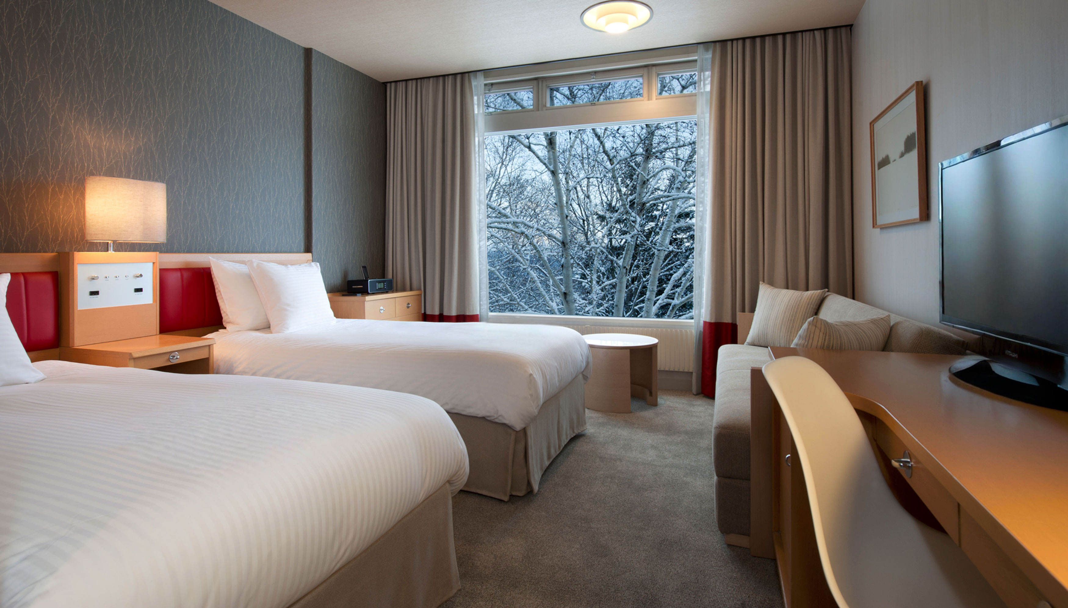 a room with two beds, couch, desk, and large window overlooking the snowy landscaape