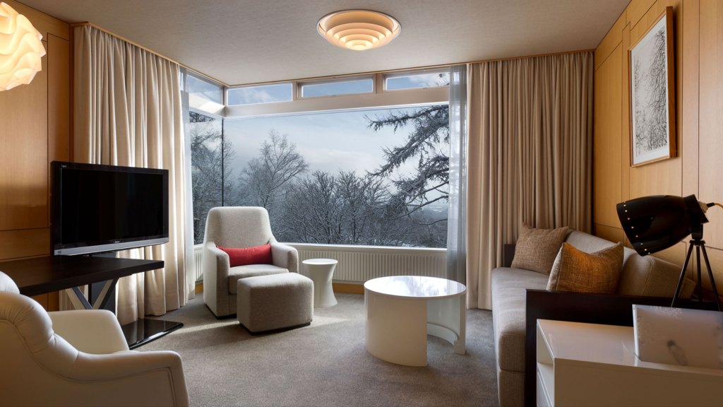 a living room with couch, chairs, tv, and large corner window.