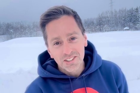 A man in a blue hooded jumper standing in the snow.