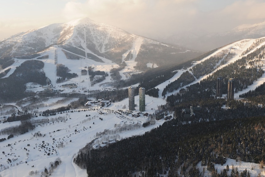 A ski field in Japan shows multiple snow-covered runs with some high-rise buildings at the base of the mountains