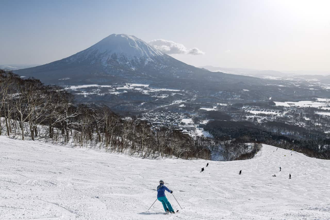People skiing down a snowy mountain, a large mountain shaped like a volcano is in the background 
