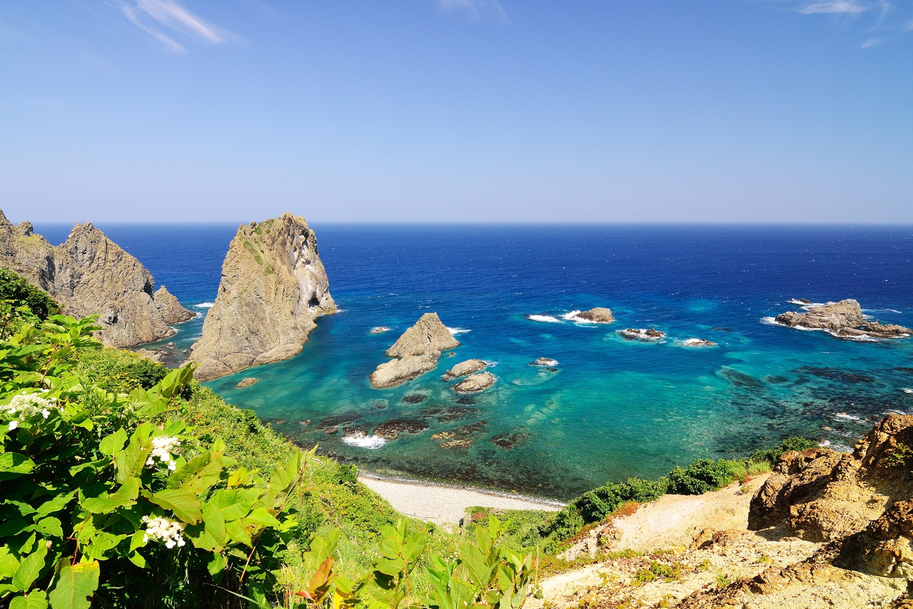 A hill-top view onto a beach with crystal clear water and cliffs emerging from the shore.