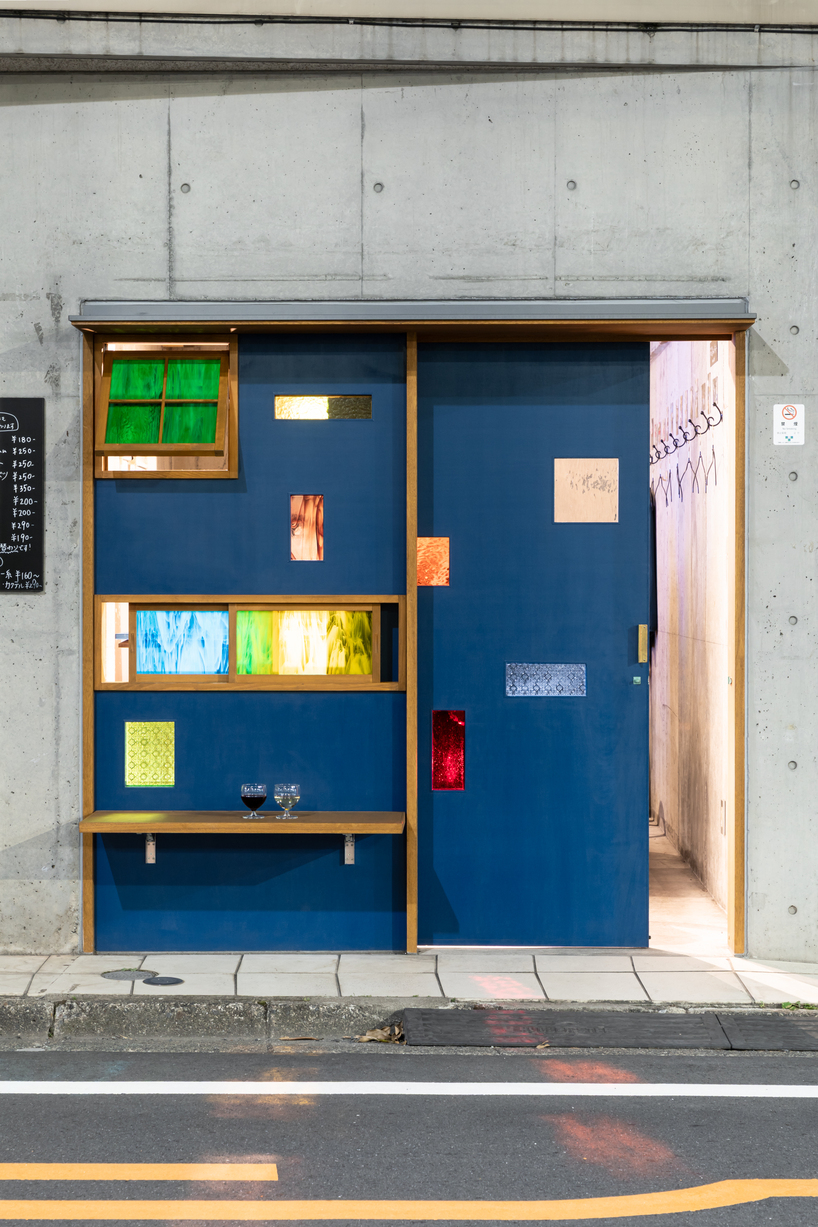 colored glass apertures reveal lively tokyo bar through bright blue entrance