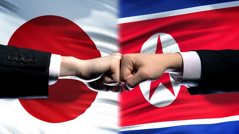 Japan vs North Korea conflict, international relations, fists on flag background