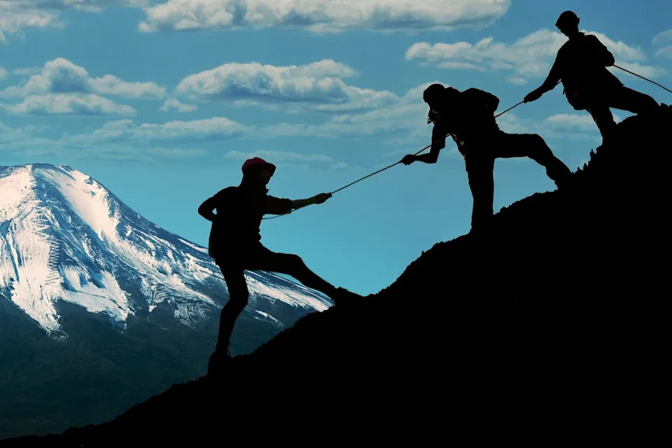 Three hikers climbing up on the peak of a mountainCredit: Getty