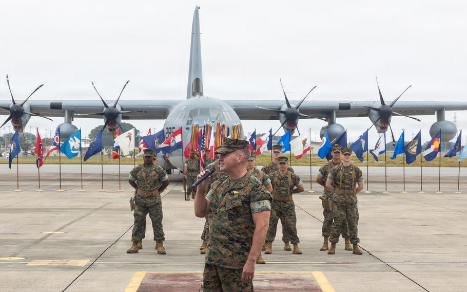 Simon Doran stands with a microphone in front of troops and a plane.