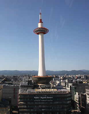 The Kyoto Tower, a thin structure painted in white and red, shoots up against a blue sky.