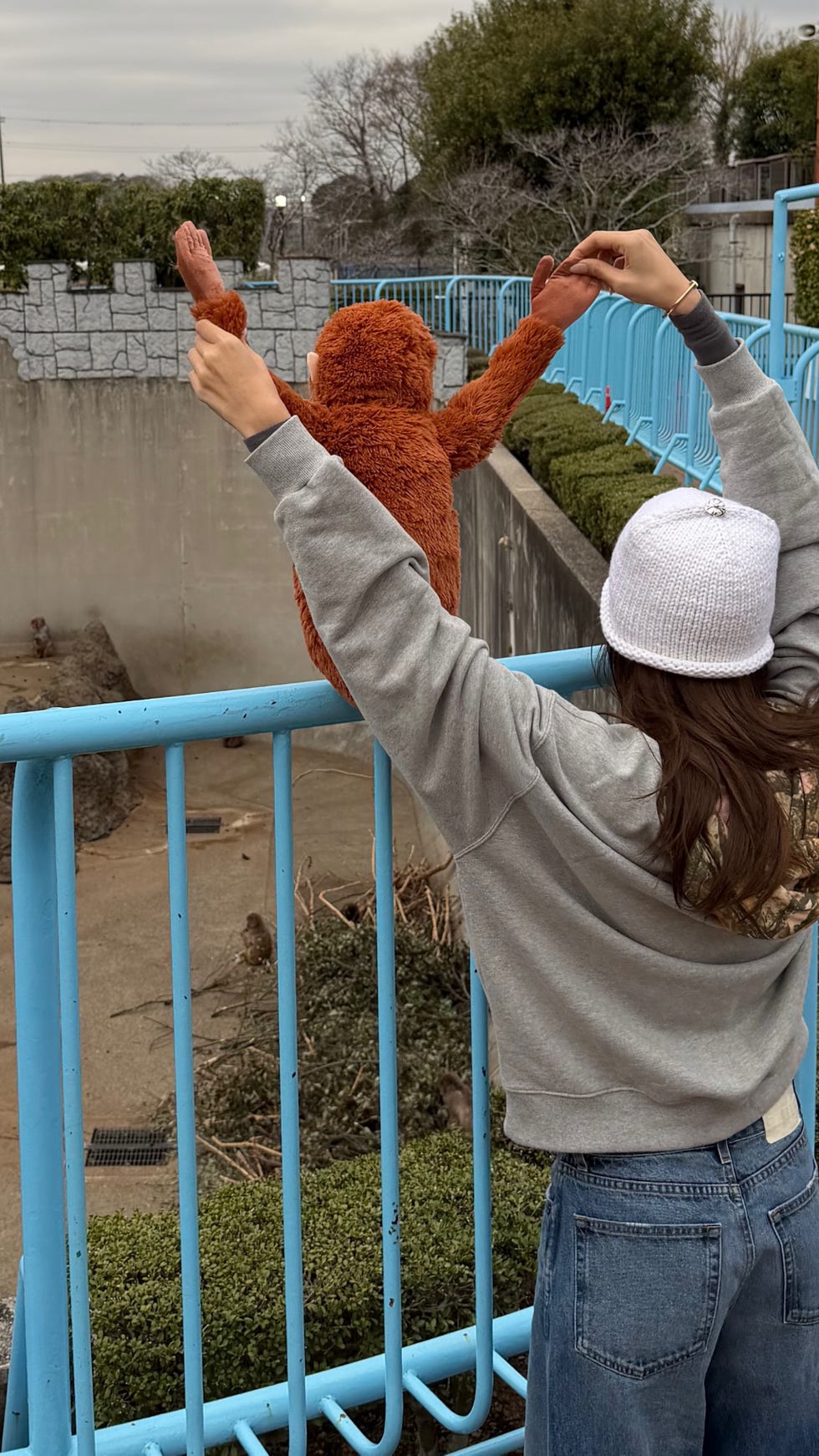 Individual holding a stuffed animal near a railing at a zoo.