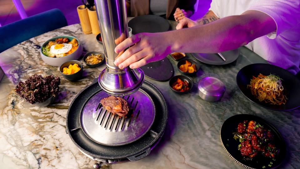 guy lowers the hood over a juicy raw piece of meat grilled at Korean restaurant to grill for his girlfriend