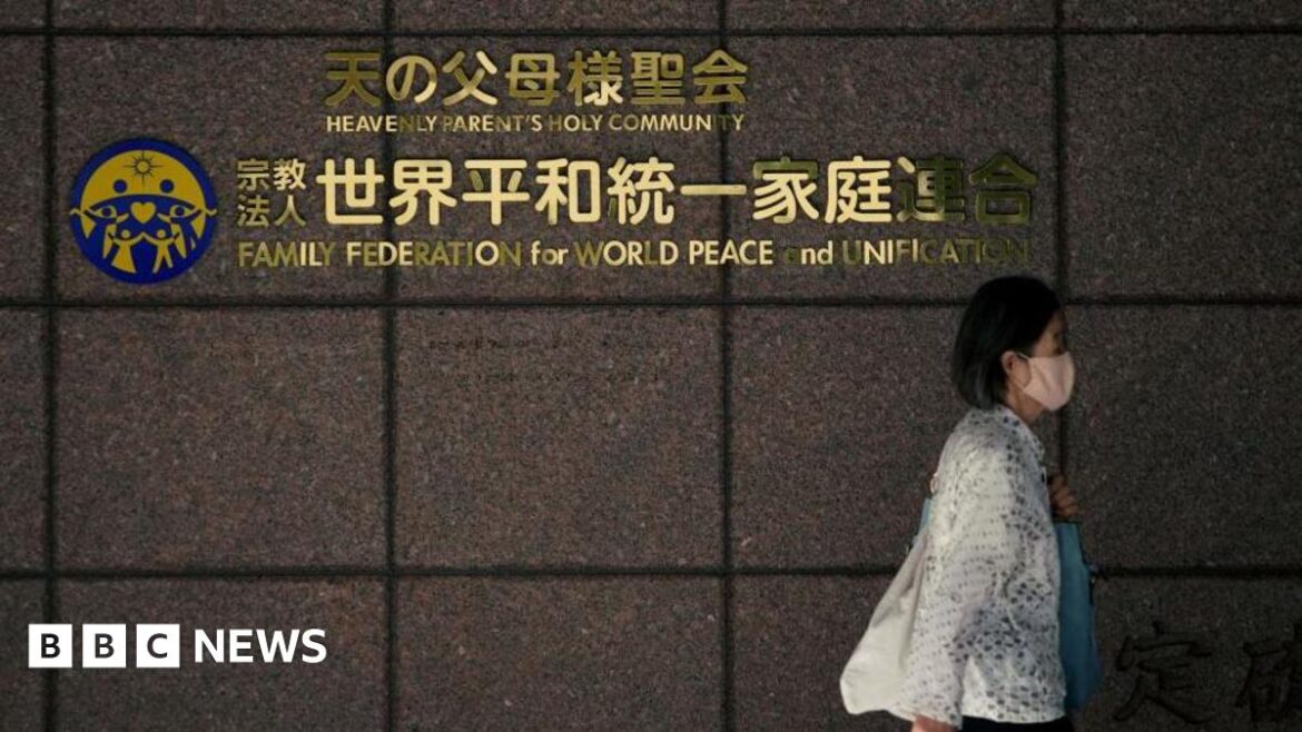 Woman wearing white walking past a wall with a sign of the Unification Church in Japan