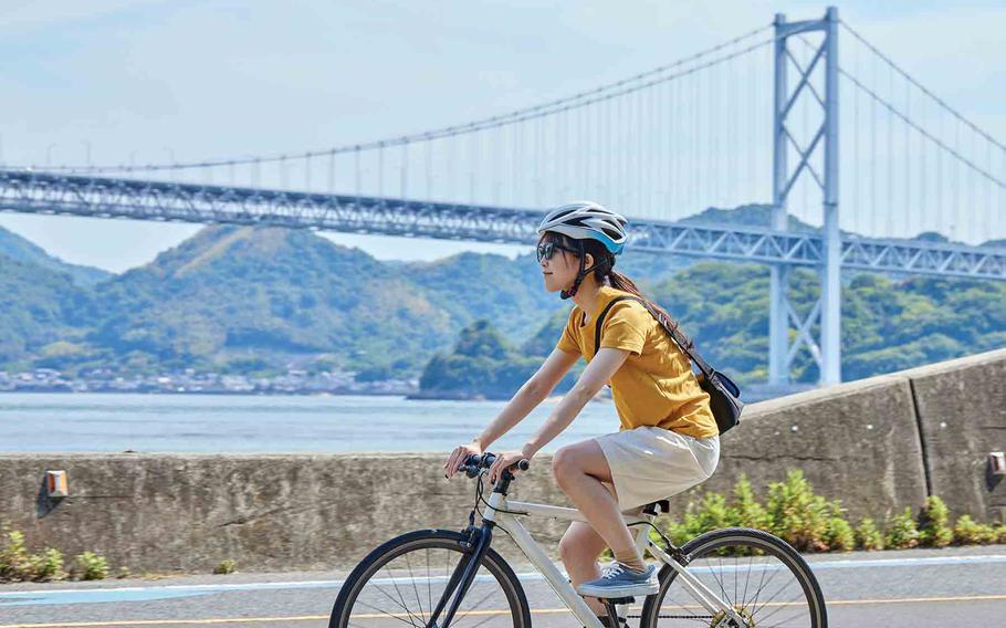 A woman cycling by the Seto Inland Sea; a bridge in the background.
