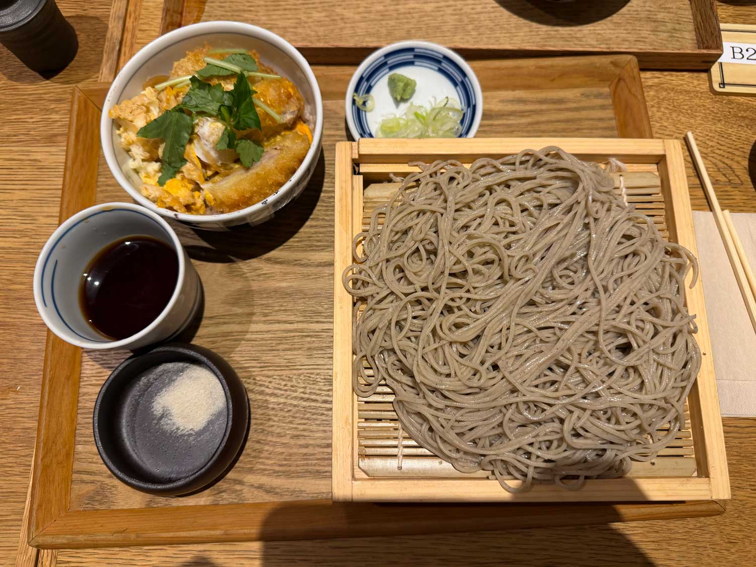 Japanese soba noodles on a bamboo tray with dipping sauce and a small bowl of chicken and egg rice.