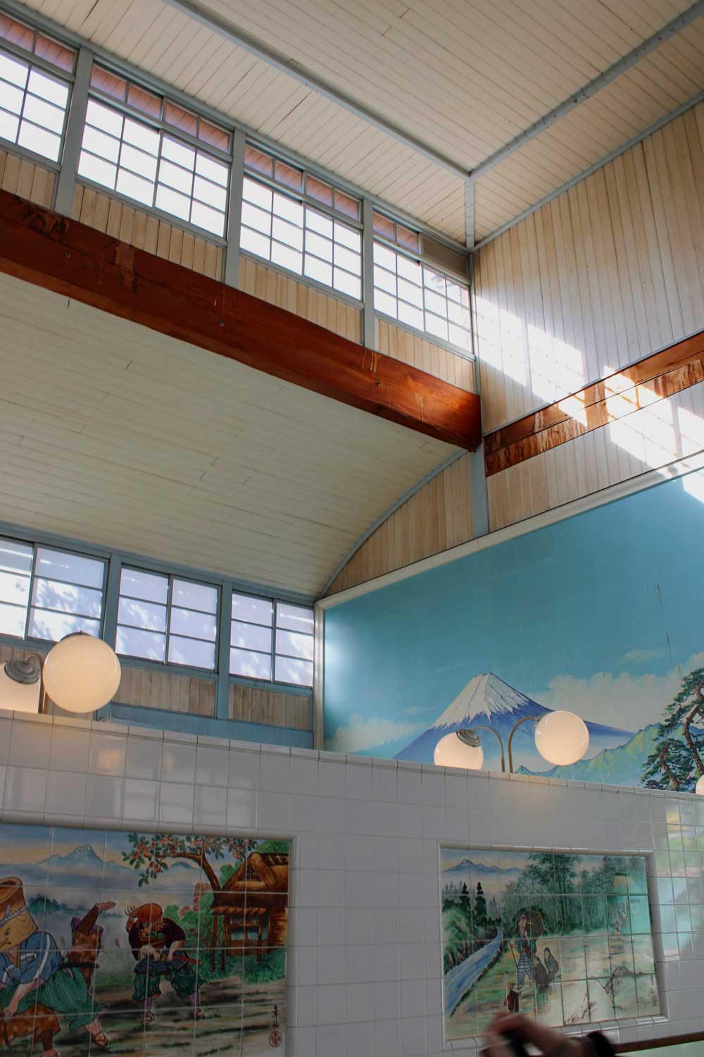 Japanese bathhouse interior with Mount Fuji mural and tall windows.