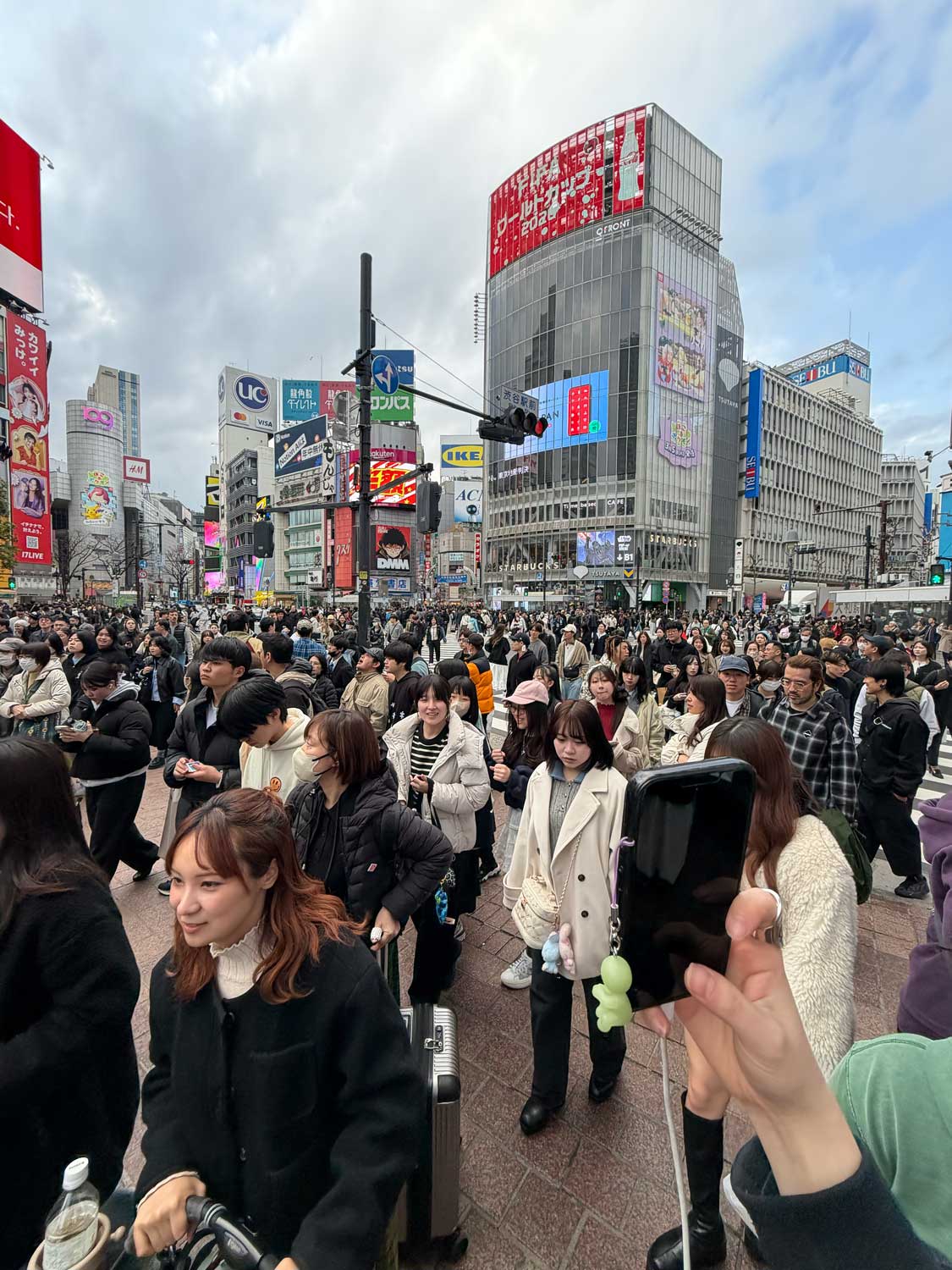 Crowds of people crossing a busy intersection surrounded by tall buildings and bright billboards in Shibuya Crossing.