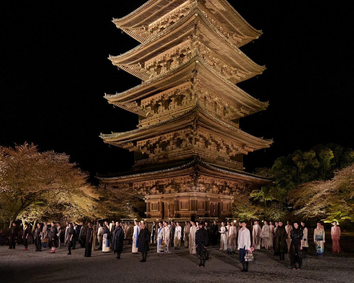 gathering of people in traditional and modern garments in front of a pagoda at night