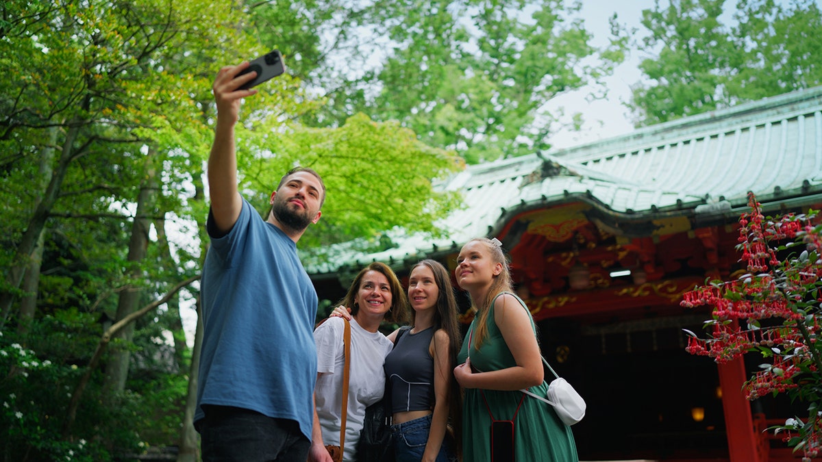 Group Of Friends Visiting Japanese Shrine and Enjoying Taking Selfies